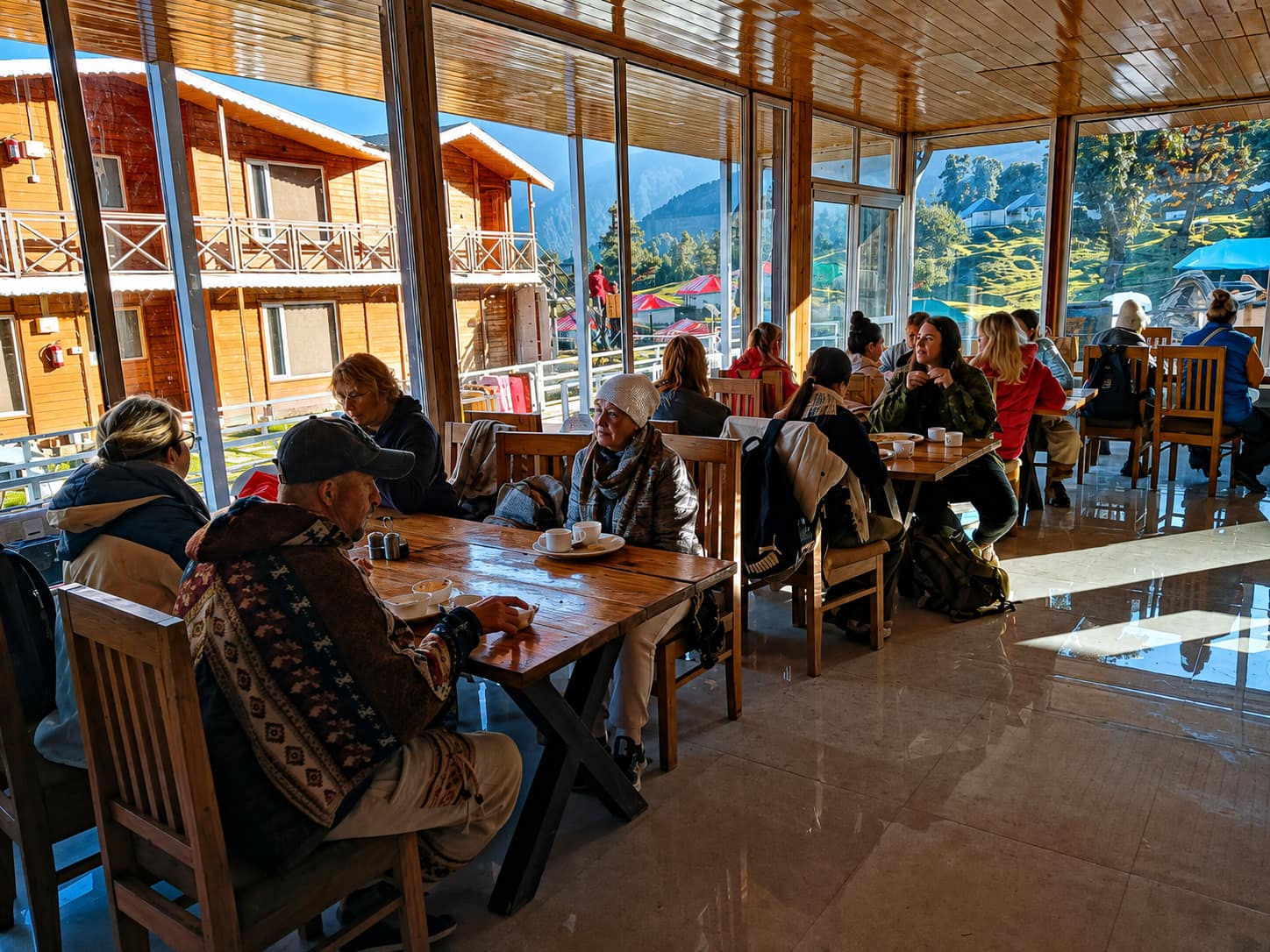 Guests dining at wooden tables beside floor-to-ceiling windows overlooking the mountains